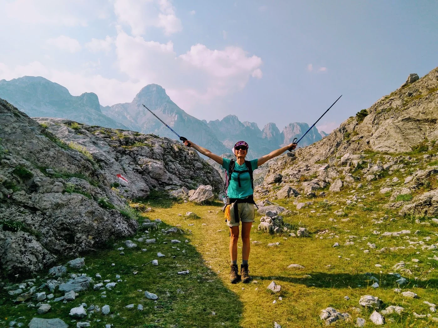 A hiker with trekking poles on a rocky path in the Albanian Alps.